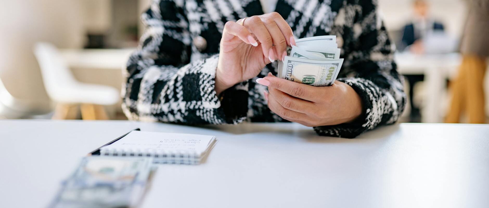 A close-up of a woman counting US dollars in an office environment, symbolizing financial management.