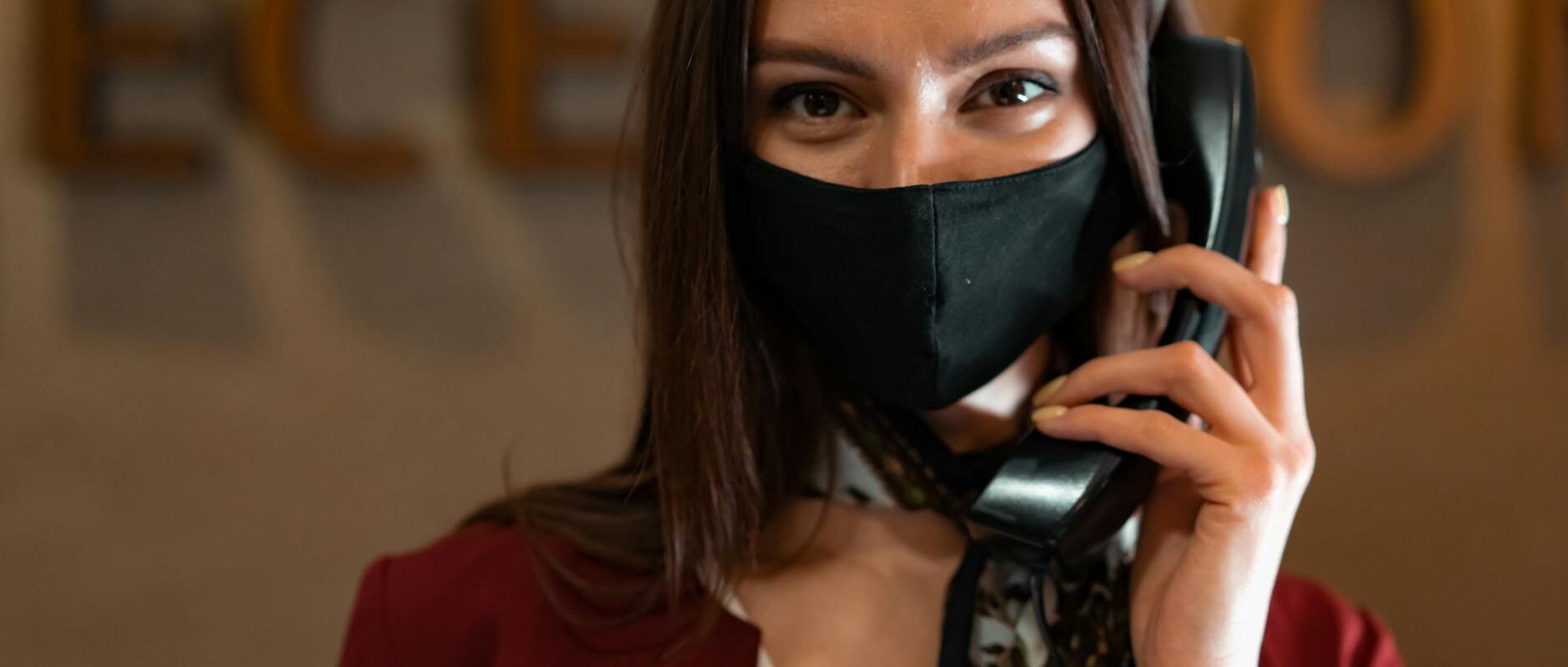 Professional woman receptionist wearing a mask while talking on the phone at the reception desk.