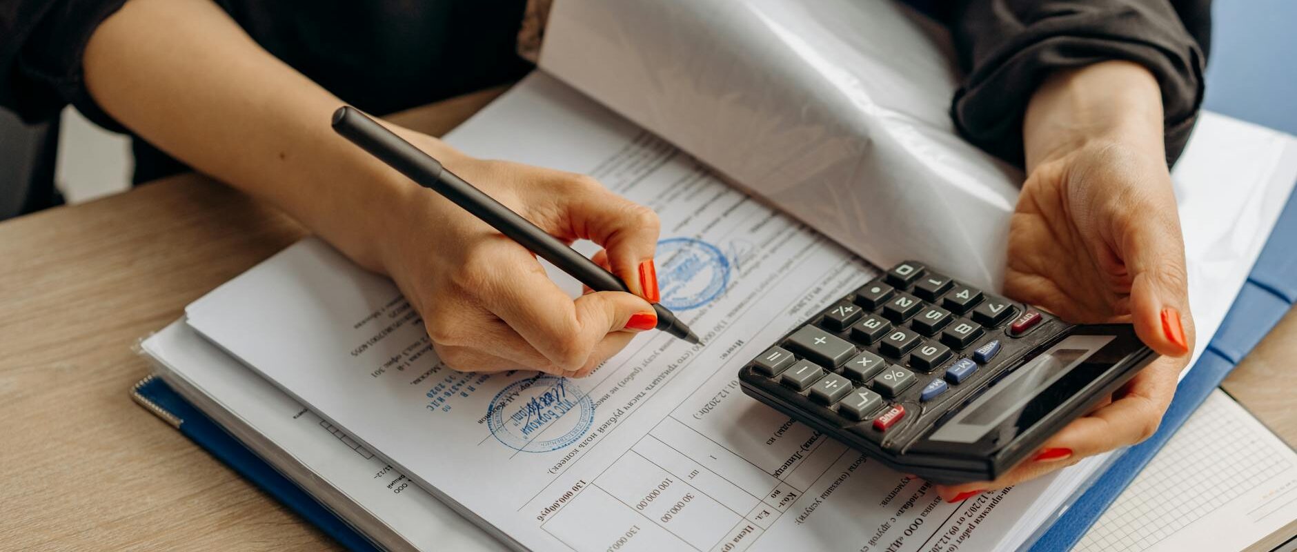 An accountant using a calculator and signing paperwork, showcasing financial analysis.