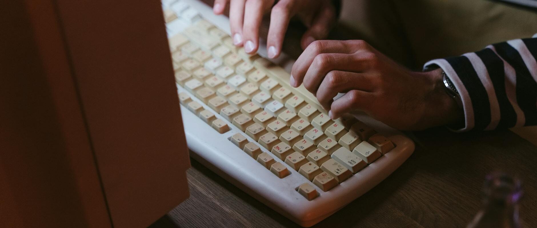Hands typing on a vintage beige keyboard with a striped sweater visible, indoors.