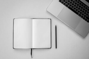 Open notebook, laptop and pen on desk, planning a virtual assistant hire