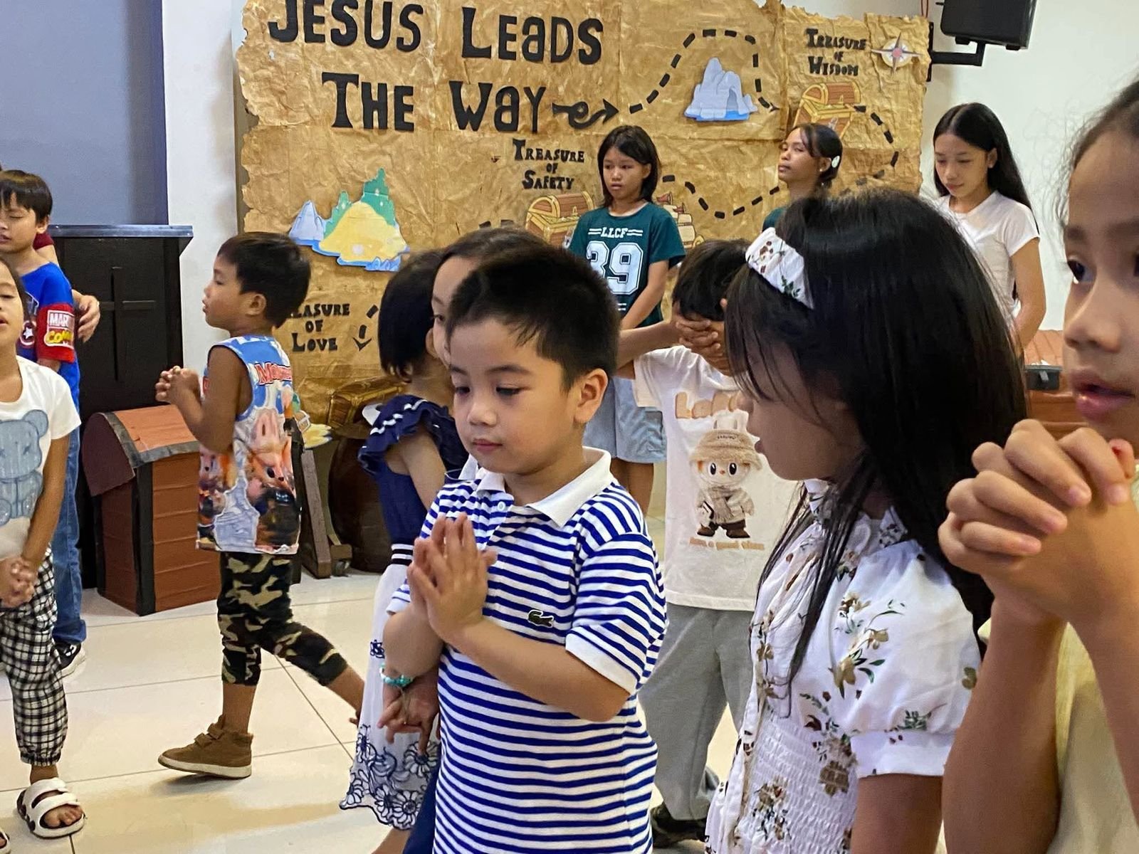 Children praying in front of the Jesus Leads the Way treasure map backdrop