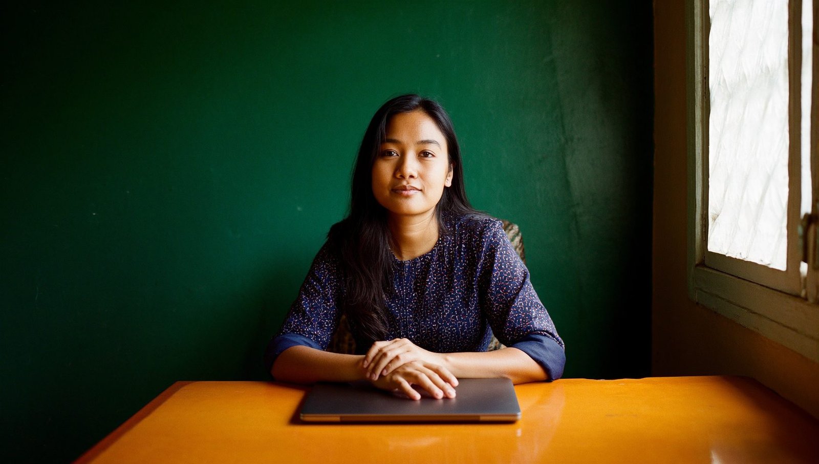 A Filipina virtual assistant seated at a desk with her hands resting on a closed laptop, looking directly at the camera