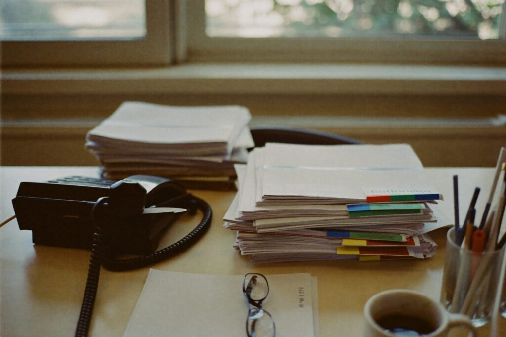 Desk in an independent insurance agency with stacked policy folders, an office phone, and reading glasses