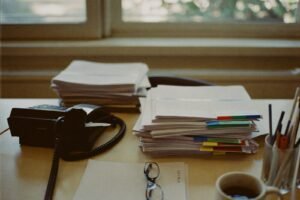 Desk in an independent insurance agency with stacked policy folders, an office phone, and reading glasses