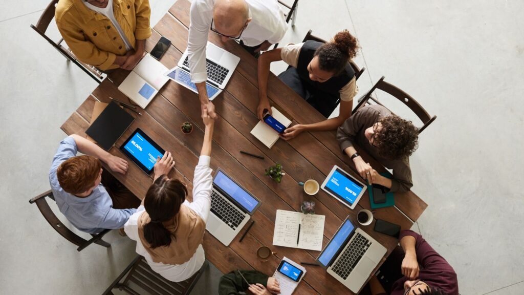 Overhead view of a business team around a table with laptops as two people shake hands across it