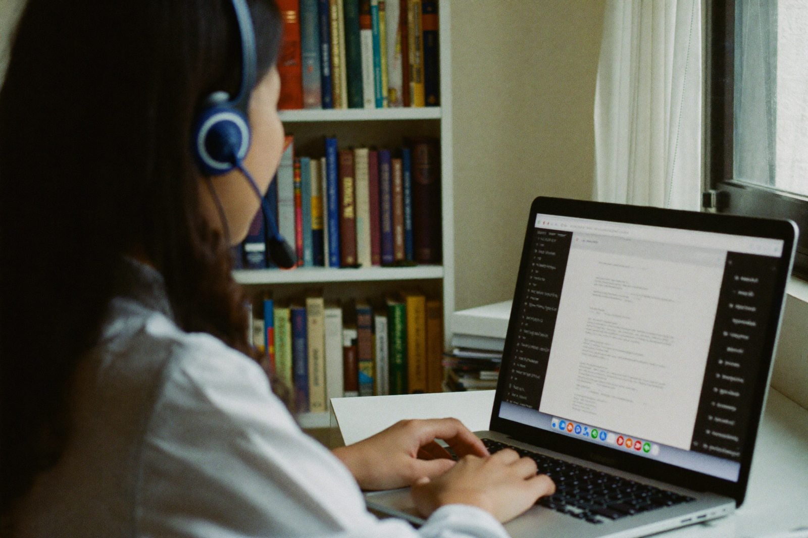 Remote legal virtual assistant with a headset working on a laptop beside a bookshelf