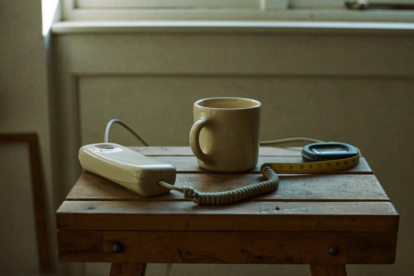 Cordless phone handset on a tradesperson's workshop bench beside a mug