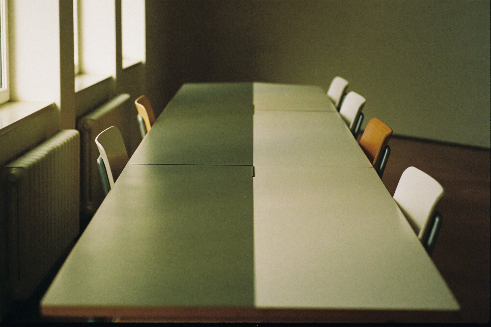 Empty meeting table with chairs tucked in, morning light through tall windows